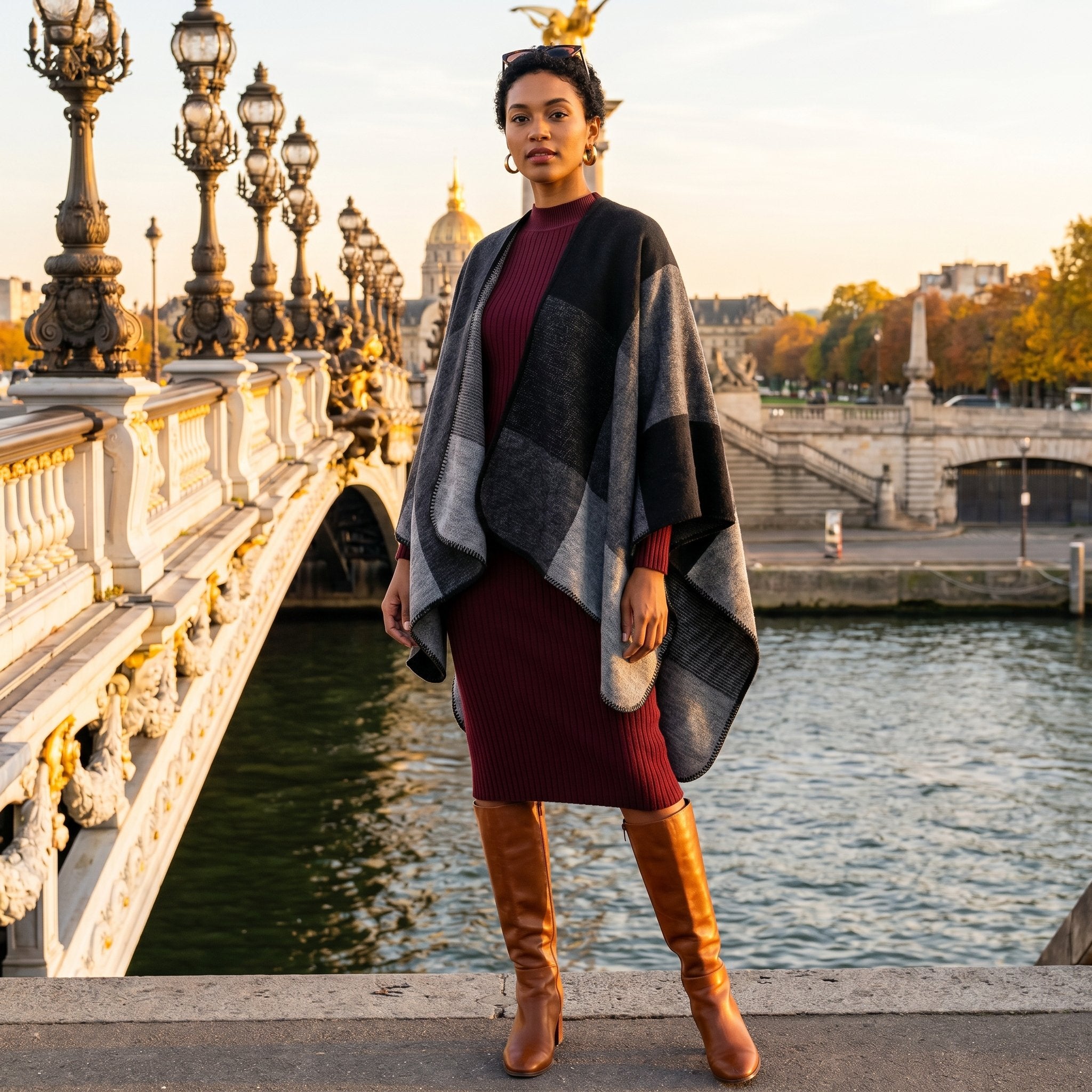 Poncho plaid colorblock gris porté par une femme posant sur un pont en pierre au bord de l'eau.