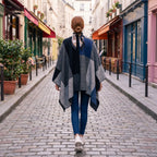 Poncho plaid colorblock gris porté par une femme vue de dos marchant dans une ruelle pavée.
