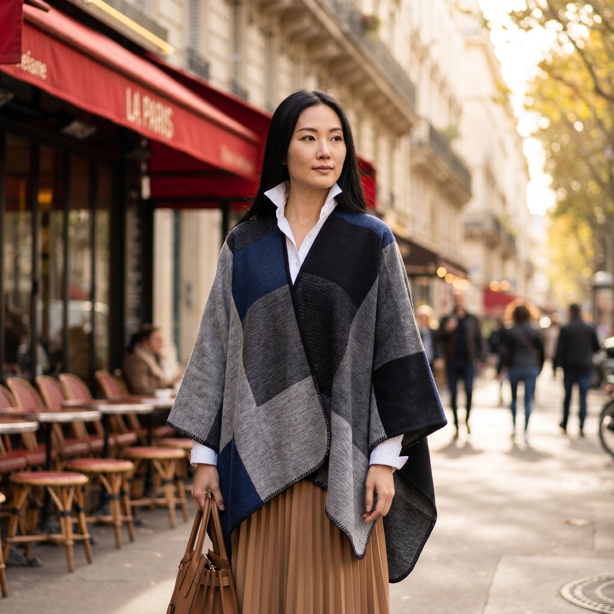 Poncho plaid colorblock gris porté par une femme posant sur un trottoir devant un café.