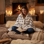 Poncho plaid motif nordique porté par une femme lisant un livre devant une cheminée allumée.