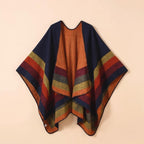 Poncho plaid à rayures bleues, oranges et rouges, étalé sur un fond beige clair et discret.