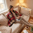 Poncho plaid tartan rouge porté par une femme souriante assise sur un canapé avec un ordinateur.