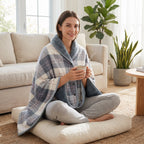Poncho polaire à carreaux gris et blanc porté par une femme assise en tailleur sur un coussin au sol.