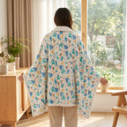 Poncho polaire à capuche motif dinosaures, porté de dos par une personne devant une fenêtre.