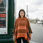 Poncho pull femme à capuche cuivre, porté par une femme souriante, vue de face en milieu urbain.