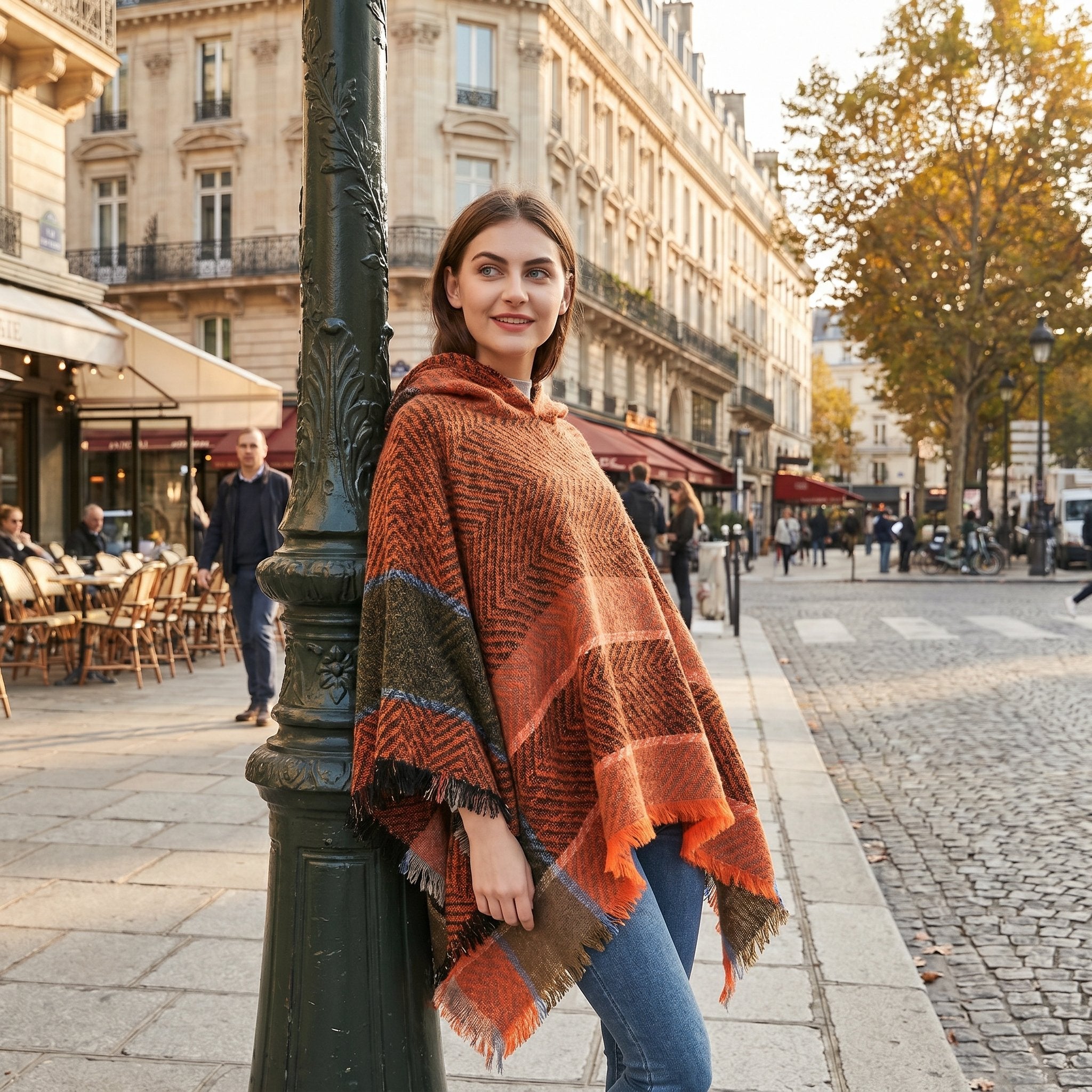 Poncho pull femme à capuche cuivre, porté par une femme appuyée contre un lampadaire en ville.