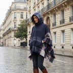 Poncho pull femme à capuche marine, porté par une femme marchant dans une rue pavée.