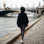 Poncho pull femme bleu marine, porté par une femme vue de dos marchant le long d'une berge.