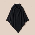 Poncho pull femme col roulé noir, posé à plat sur un fond clair et neutre.