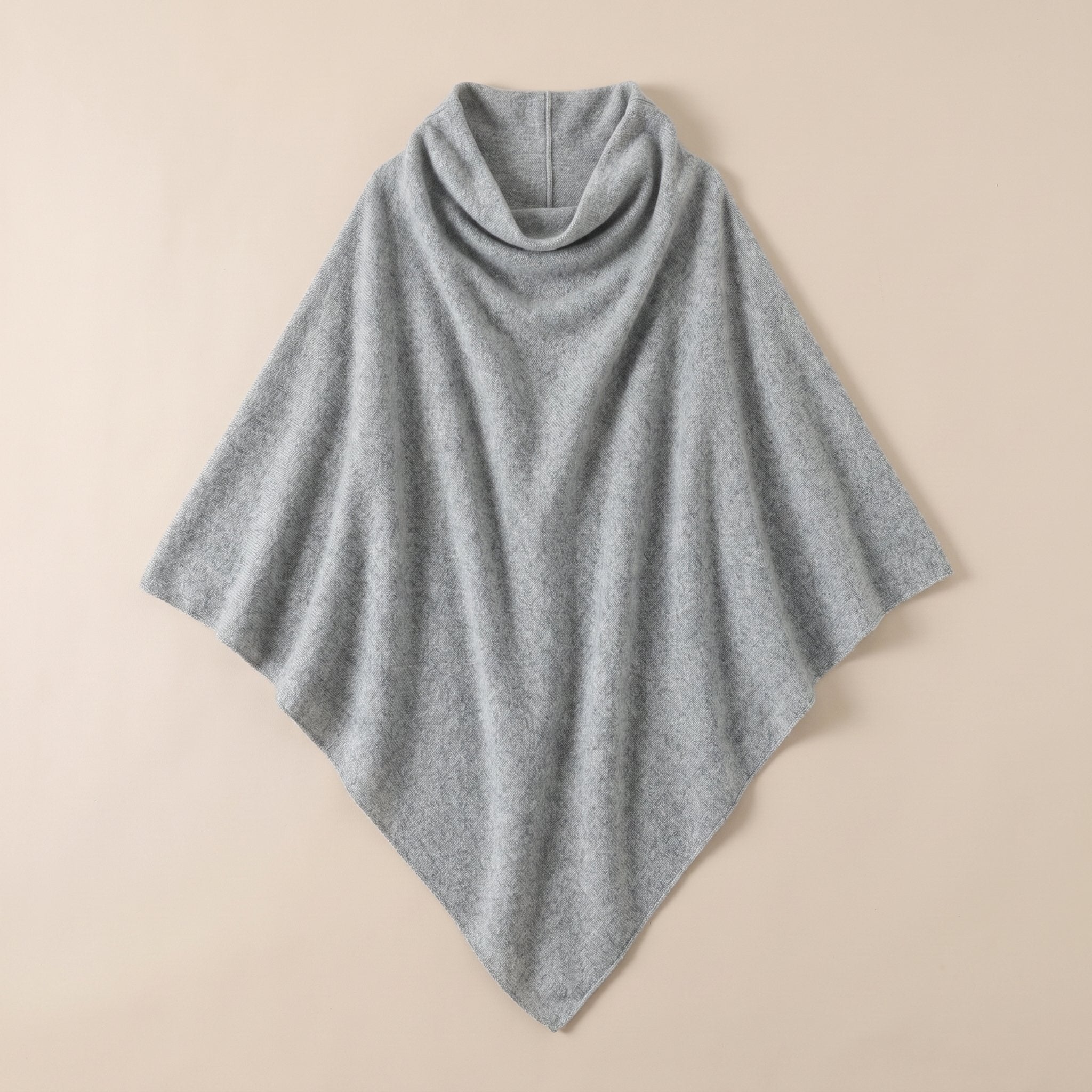 Poncho pull femme col roulé gris clair, étalé à plat sur un fond beige uni.