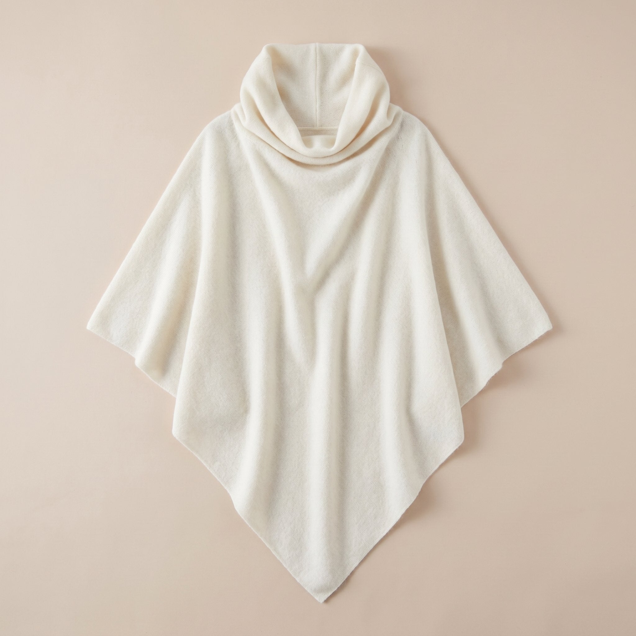 Poncho pull femme col roulé blanc cassé, disposé à plat sur un fond neutre.