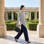 Poncho pull femme gris clair porté par une femme marchant dans une cour à colonnes.