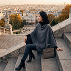 Poncho pull femme gris foncé porté par une femme assise sur des marches en pierre.