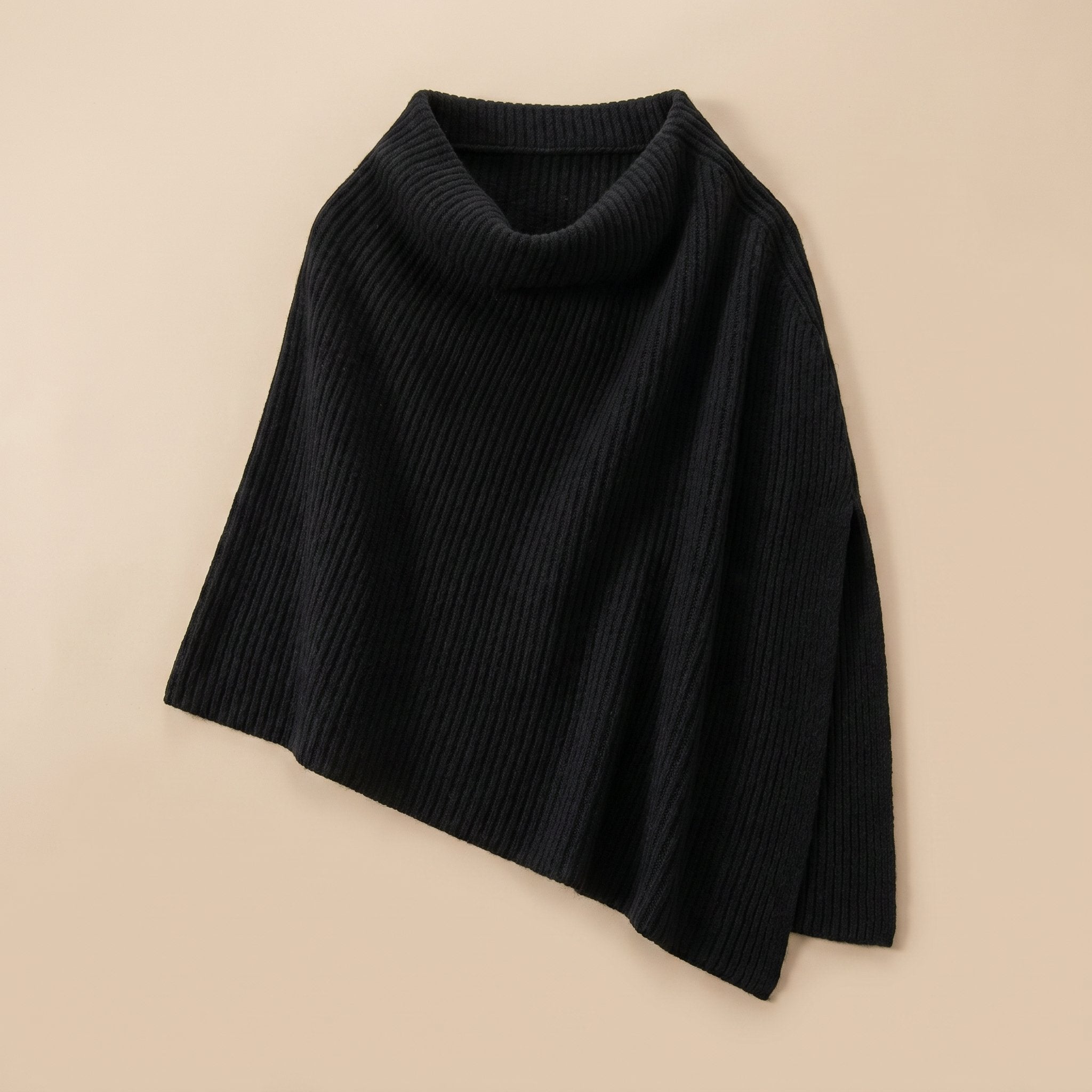 Poncho pull femme couleur noire, posé à plat, mettant en valeur sa coupe asymétrique.