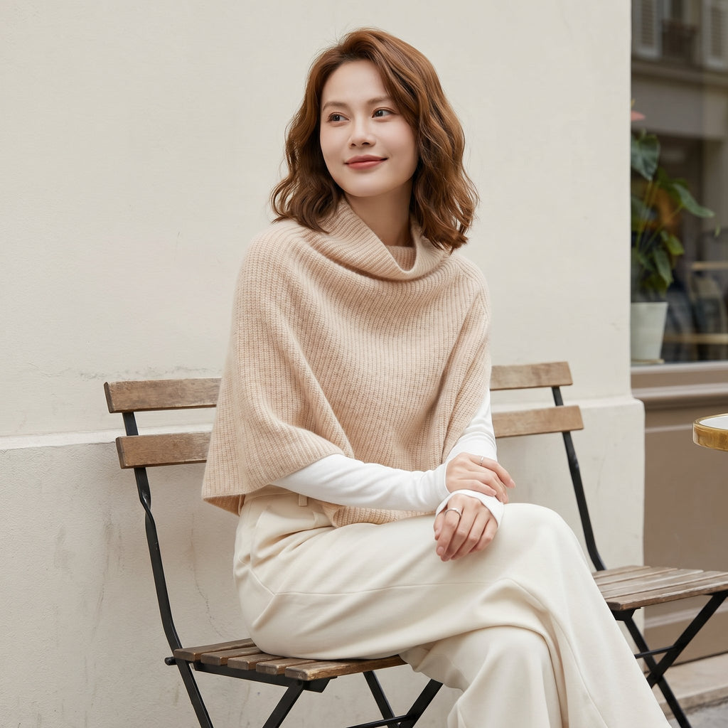 Poncho pull femme couleur beige, porté par une femme assise en extérieur, vue de profil, regardant sur le côté.