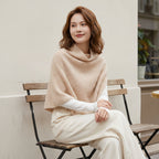 Poncho pull femme couleur beige, porté par une femme assise en extérieur, vue de profil, regardant sur le côté.