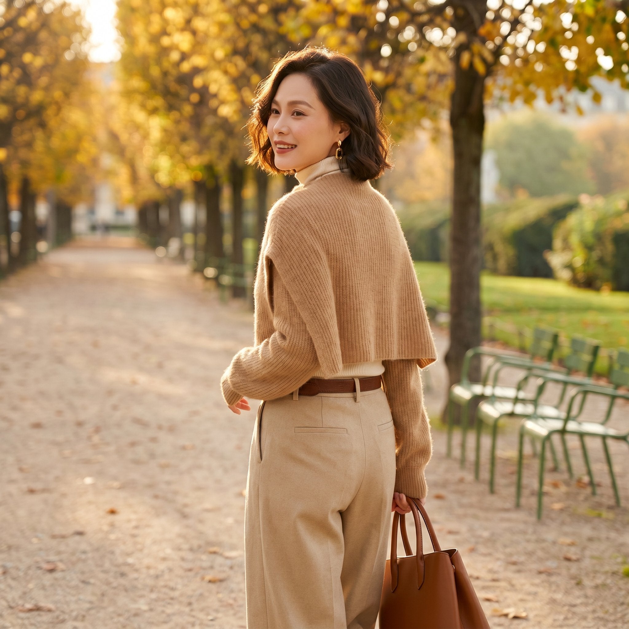 Poncho pull femme beige, porté par une femme de dos marchant dans une allée de parc.