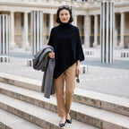Poncho pull femme col roulé noir, porté par une femme descendant des marches, tenant un manteau.