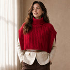 Poncho pull femme maille torsadée rouge, porté par une femme en intérieur, cadrage mi-corps.