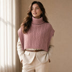 Poncho pull femme maille torsadée rose, porté par une femme en intérieur, vue frontale.
