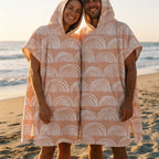 Poncho serviette a capuche motif Arches pêche, porté par un homme et une femme côte à côte, souriant sur la plage.