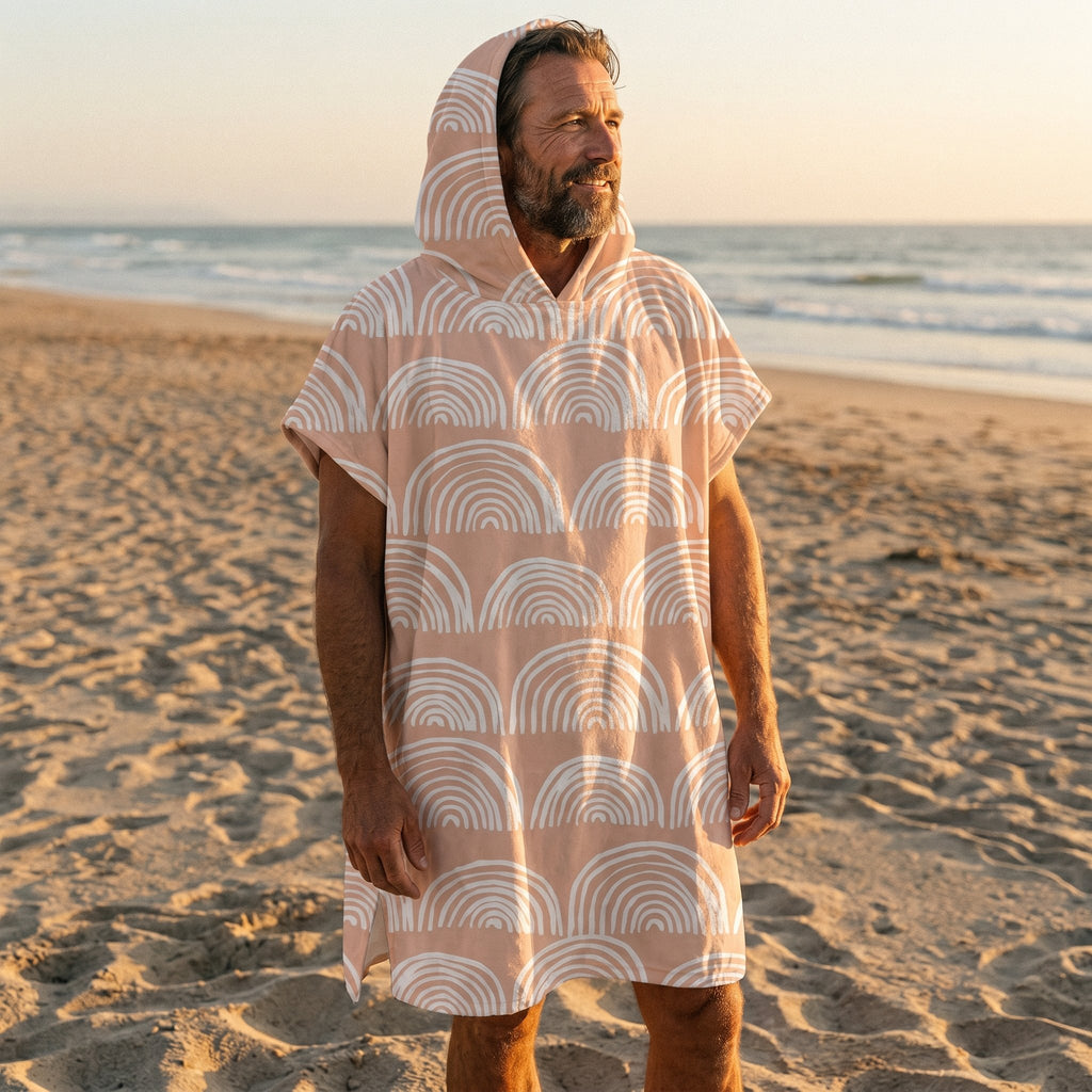 Poncho serviette a capuche motif Arches pêche, porté par un homme debout sur le sable, regardant vers l'horizon marin.