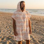 Poncho serviette a capuche motif Arches pêche, porté par un homme debout sur le sable, regardant vers l'horizon marin.