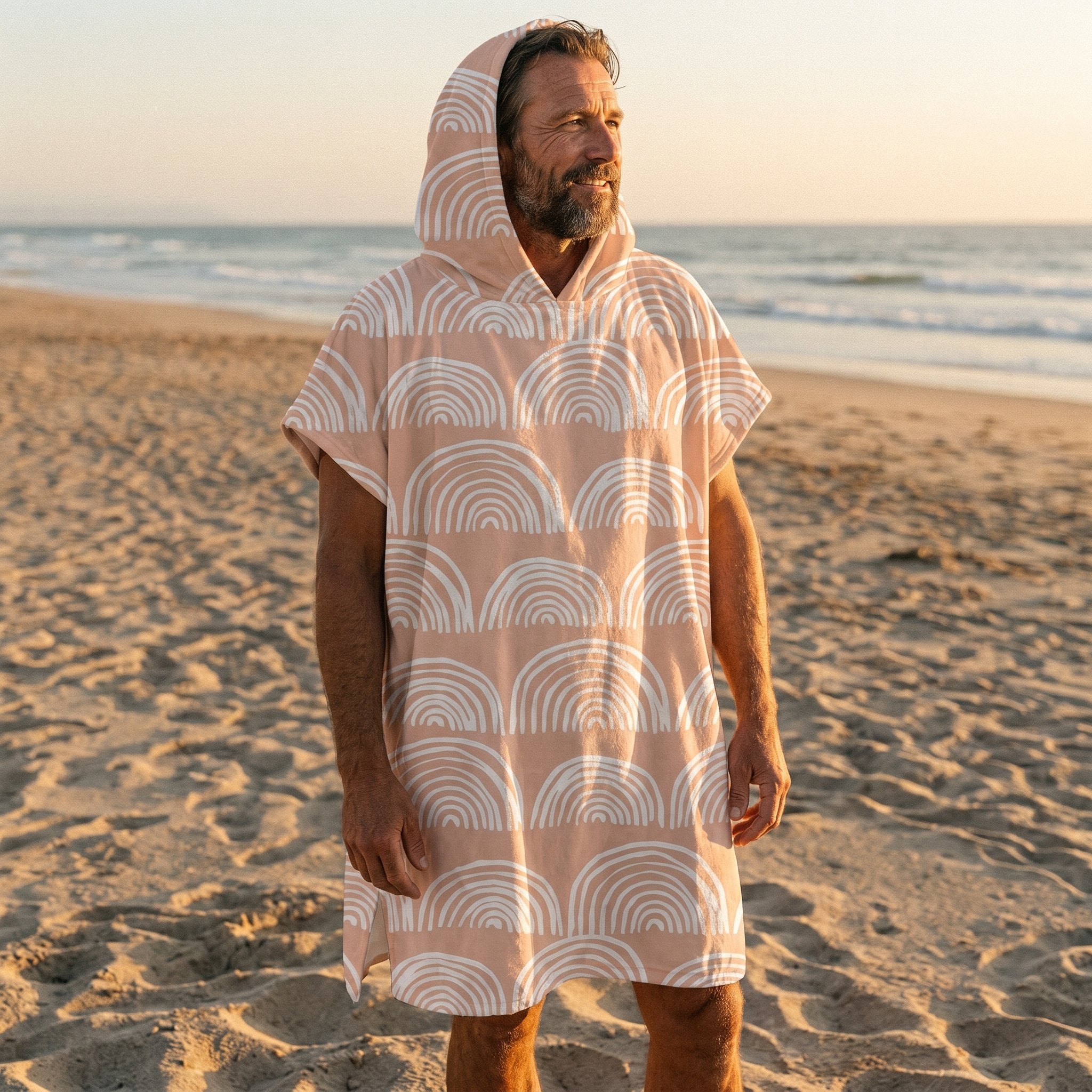 Poncho serviette a capuche motif Arches pêche, porté par un homme debout sur le sable, regardant vers l'horizon marin.