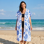 Poncho serviette à capuche motif coquillages bleus, porté ouvert par une femme souriante, vue de face sur la plage.