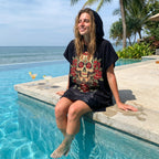 Poncho serviette à capuche motif crâne aux roses rouges, porté par une femme assise au bord d'une piscine.