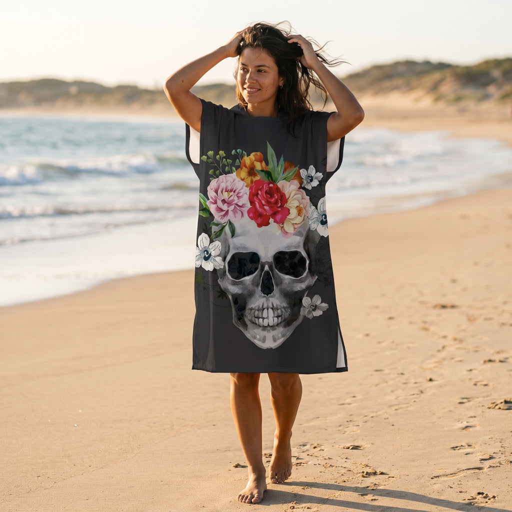 Poncho serviette à capuche motif crâne couronne de fleurs, porté par une femme marchant sur la plage.
