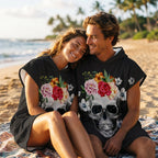 Poncho serviette à capuche motif crâne couronne de fleurs, porté par un couple souriant assis sur la plage.