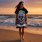 Poncho serviette a capuche motif crâne et roses violettes, porté par une femme marchant sur une plage au soleil couchant.