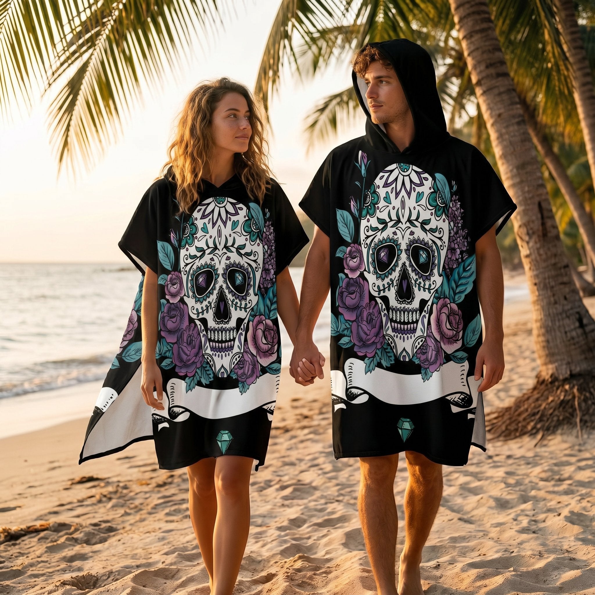 Poncho serviette a capuche motif crâne et roses violettes, porté par un couple marchant main dans la main sur une plage.
