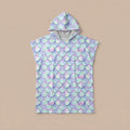 Poncho serviette a capuche motif écailles lilas, posé à plat sur un fond uni beige clair.