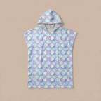 Poncho serviette a capuche motif écailles lilas, posé à plat sur un fond uni beige clair.