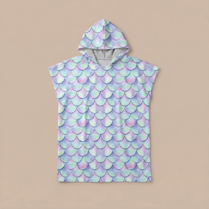 Poncho serviette a capuche motif écailles lilas, posé à plat sur un fond uni beige clair.
