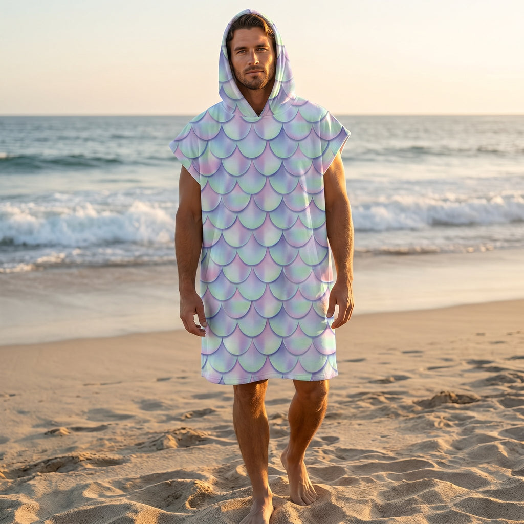 Poncho serviette a capuche motif écailles lilas, porté par un homme marchant sur le sable, la mer en arrière-plan.