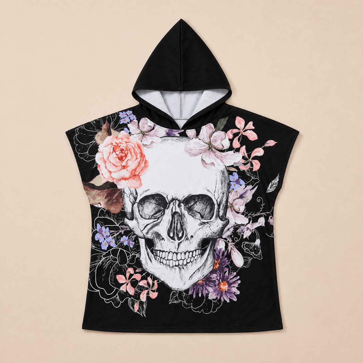 Poncho serviette a capuche motif crâne et roses pastel, vue de face, posé à plat sur un fond uni clair.