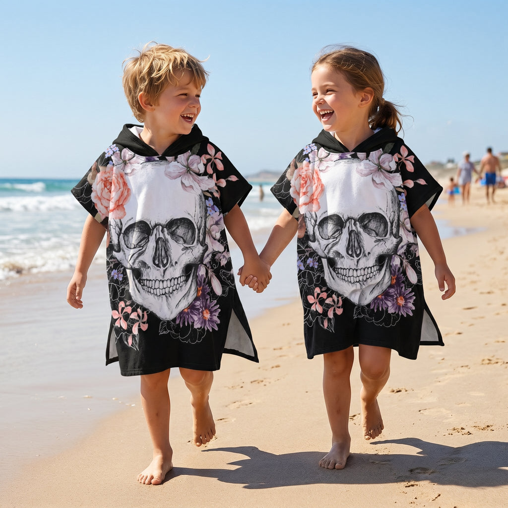 Poncho serviette a capuche motif crâne et roses pastel, portés par deux enfants joyeux qui se tiennent la main.