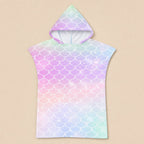 Poncho serviette a capuche motif écailles arc-en-ciel pastel, présenté à plat sur un fond beige uni.