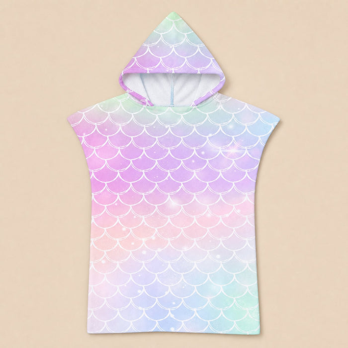 Poncho serviette a capuche motif écailles arc-en-ciel pastel, présenté à plat sur un fond beige uni.
