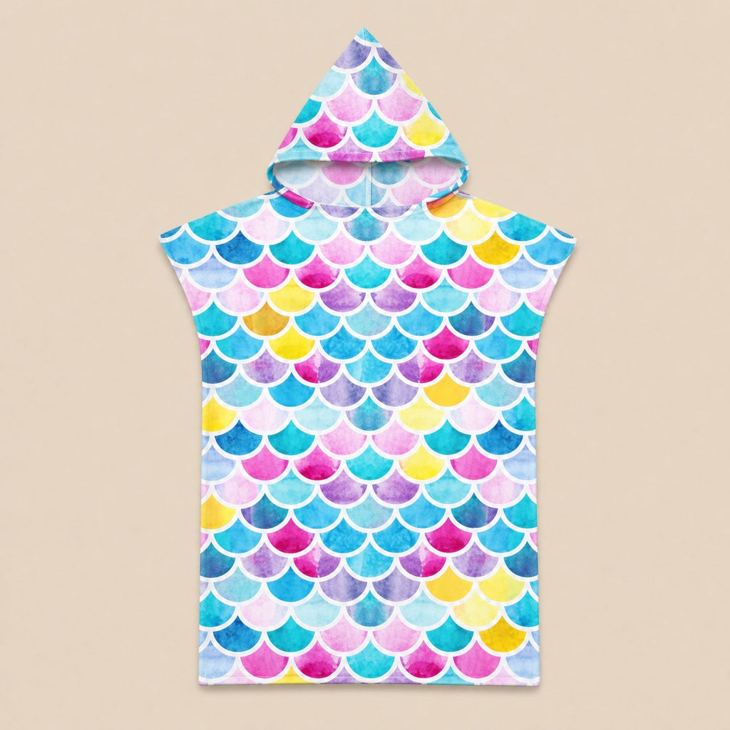 Poncho serviette à capuche motif écailles multicolores, posé à plat sur un fond beige uni.