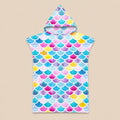 Poncho serviette à capuche motif écailles multicolores, posé à plat sur un fond beige uni.