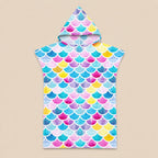 Poncho serviette à capuche motif écailles multicolores, posé à plat sur un fond beige uni.