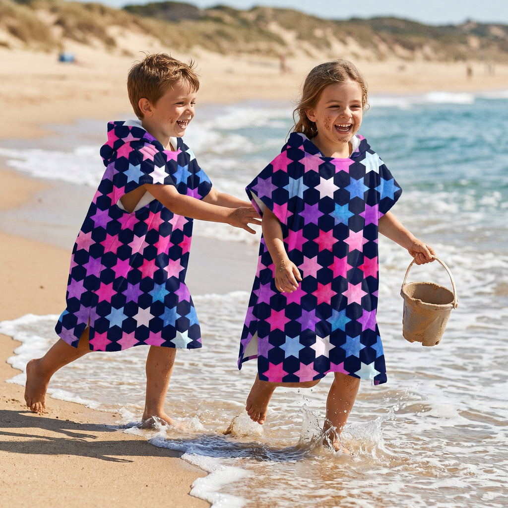 Poncho serviette à capuche enfant · Étoiles multicolores, porté par deux enfants marchant dans l'eau peu profonde de la plage