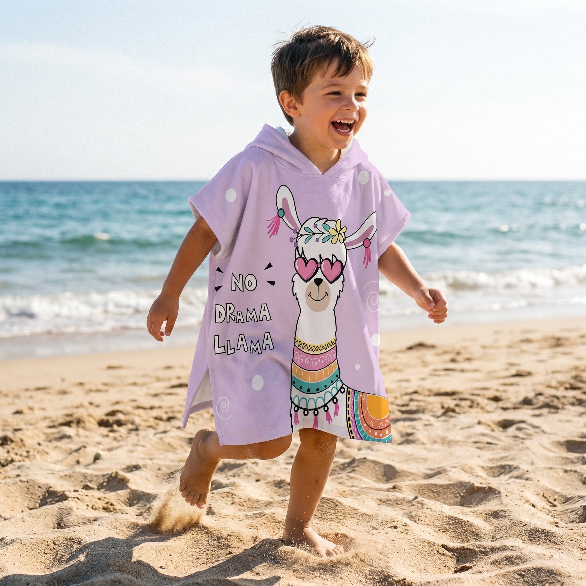 Poncho serviette a capuche motif Lama à lunettes, porté par un garçon courant joyeusement sur la plage.