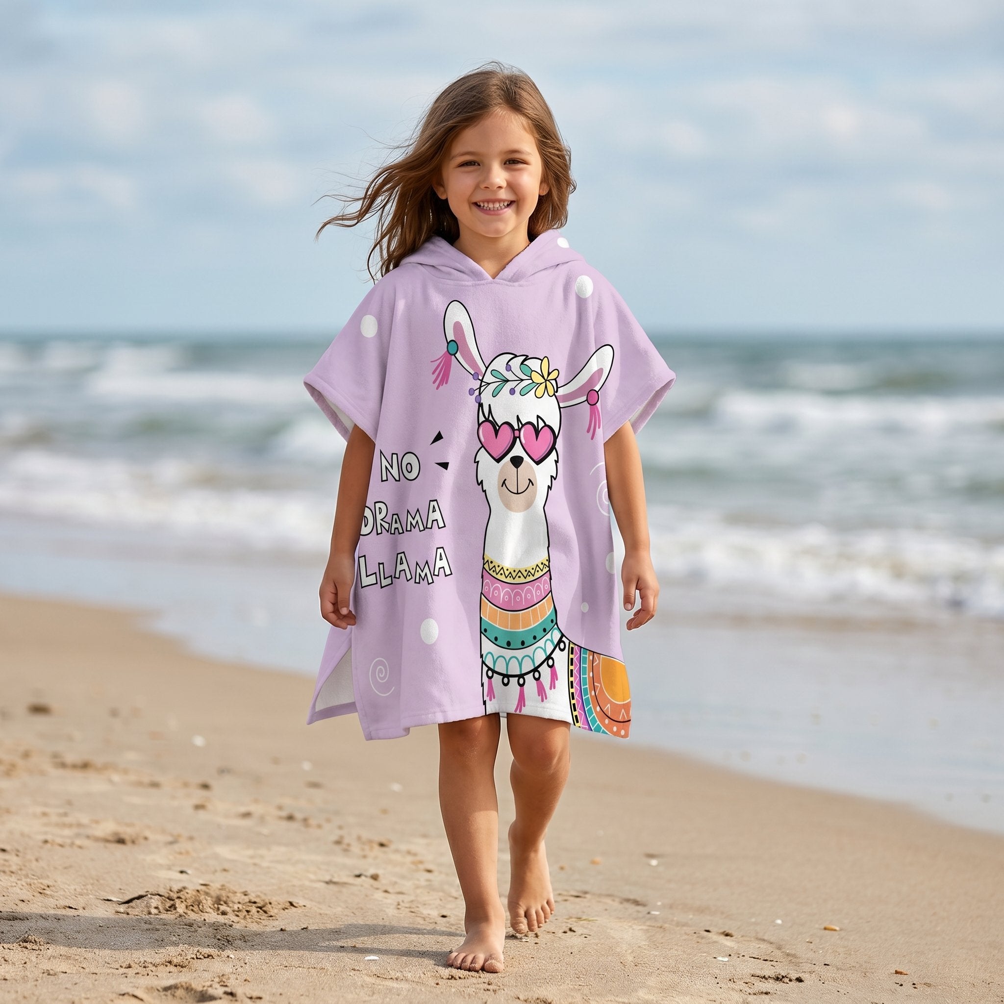 Poncho serviette a capuche motif Lama à lunettes, porté par une fille marchant sur le sable fin de la plage.