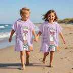 Poncho serviette a capuche motif Lama à lunettes, porté par deux enfants courant main dans la main sur la plage.