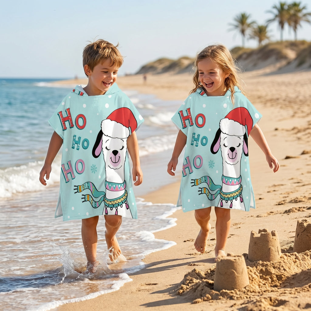Poncho serviette à capuche motif lama bonnet de Noël, porté par deux enfants marchant côte à côte sur le rivage de la plage.